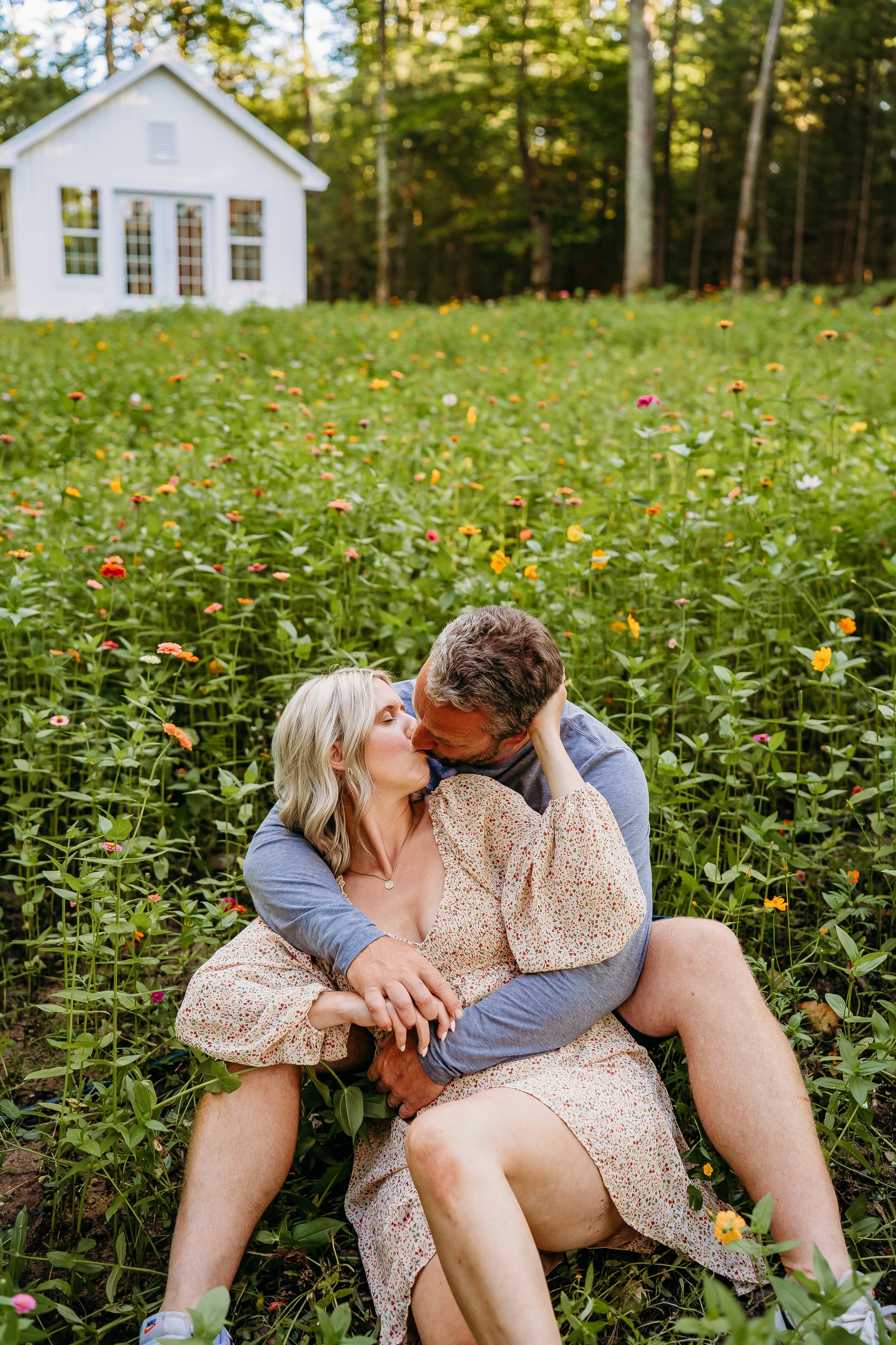 Couple embracing in the wildflower field with the white studio cottage behind