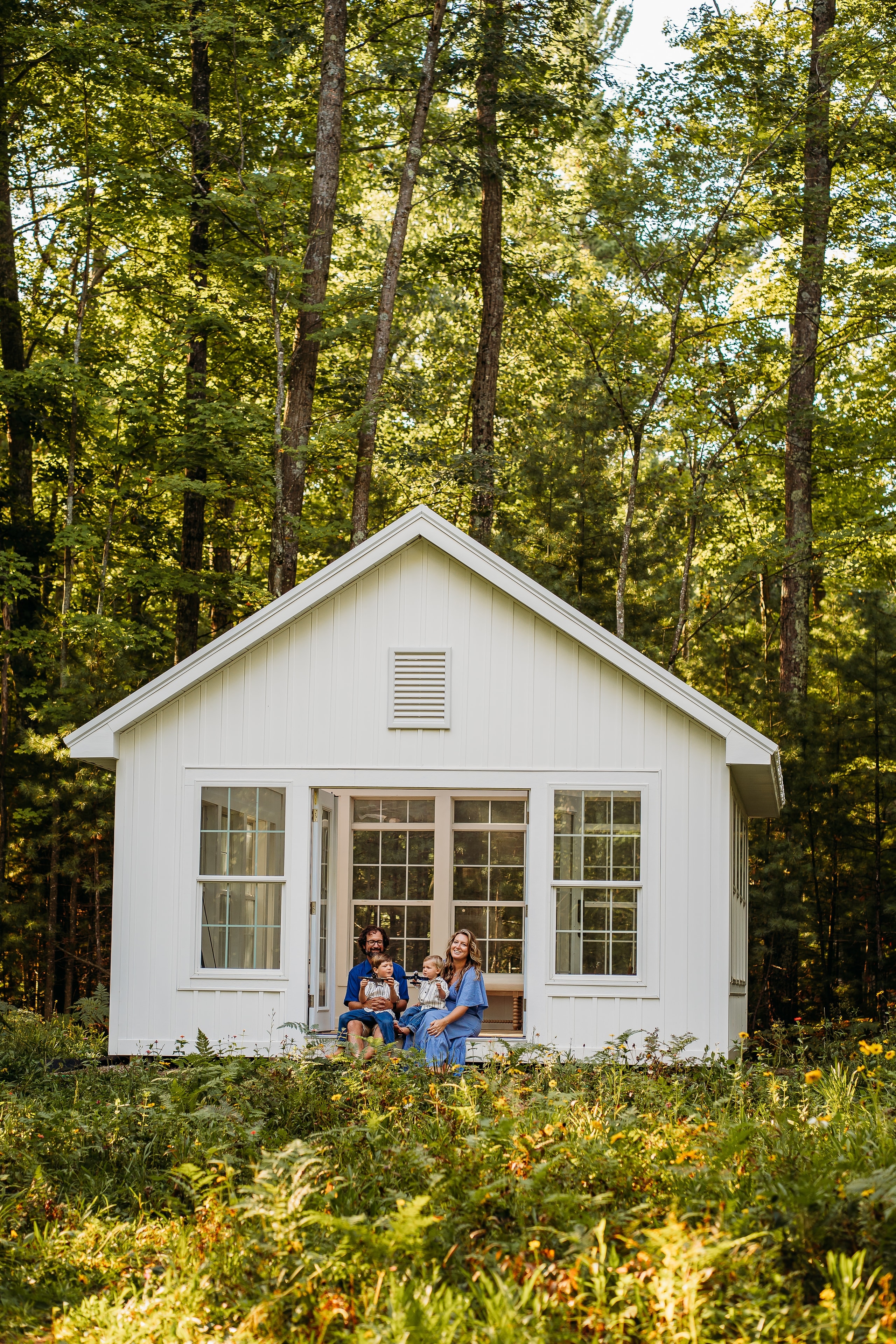 Family seated in the doorway of the white studio surrounded by wildflowers and trees