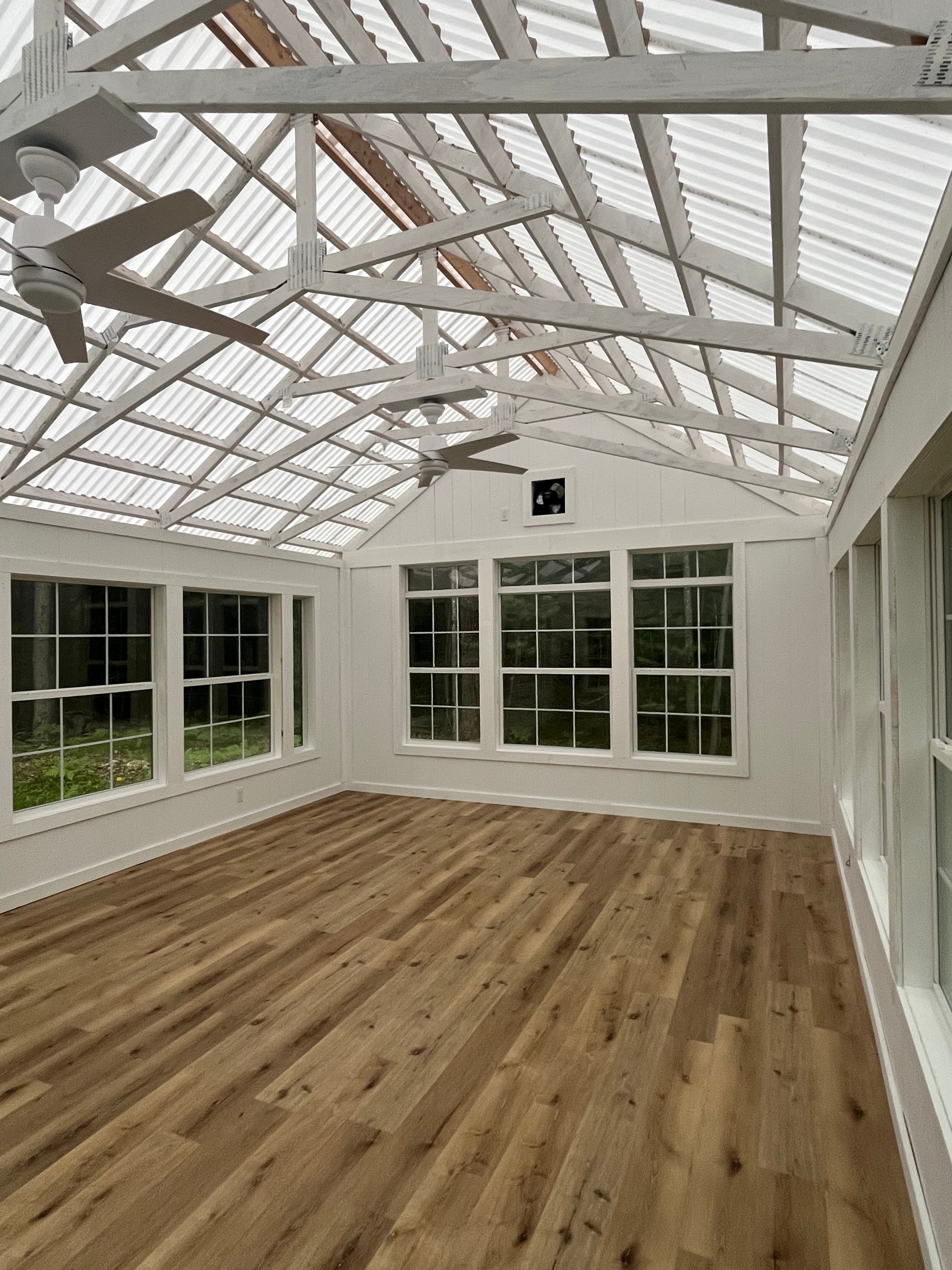 Covered porch of the studio with exposed trusses, large windows, and wood-plank floors