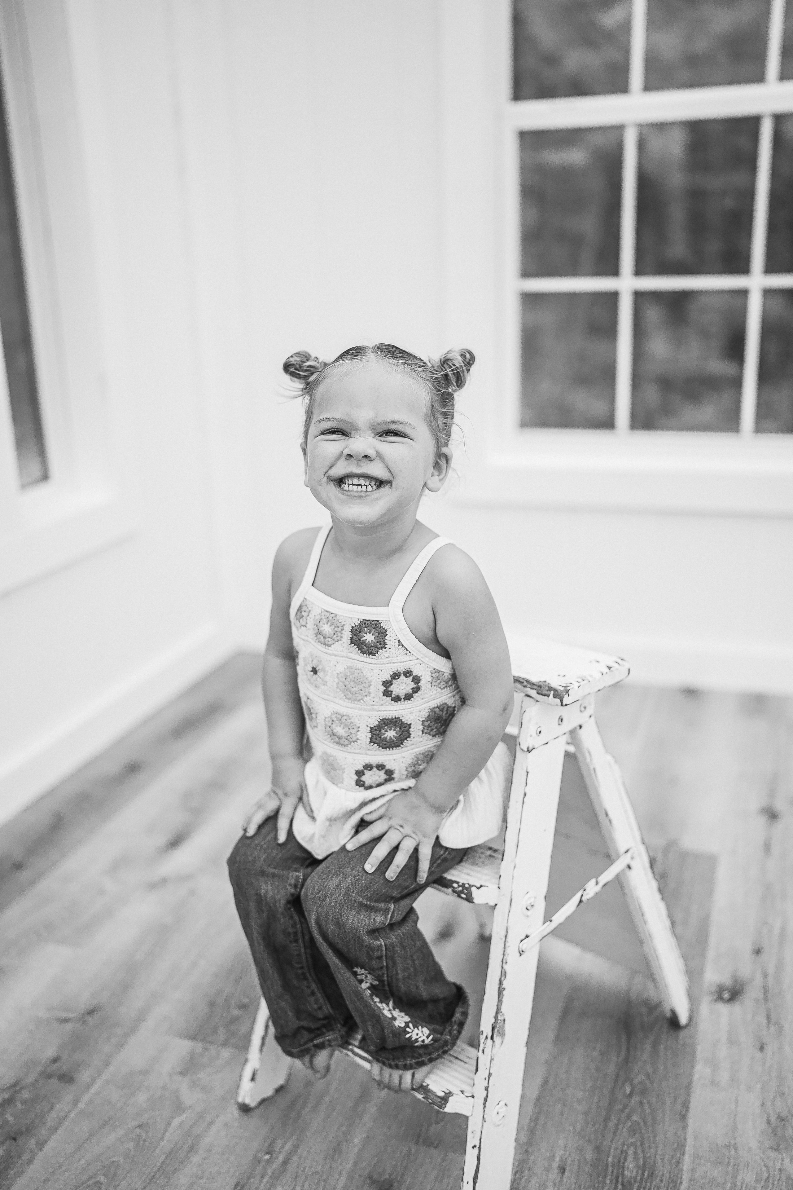 Laughing toddler girl sitting on a vintage ladder stool in the studio